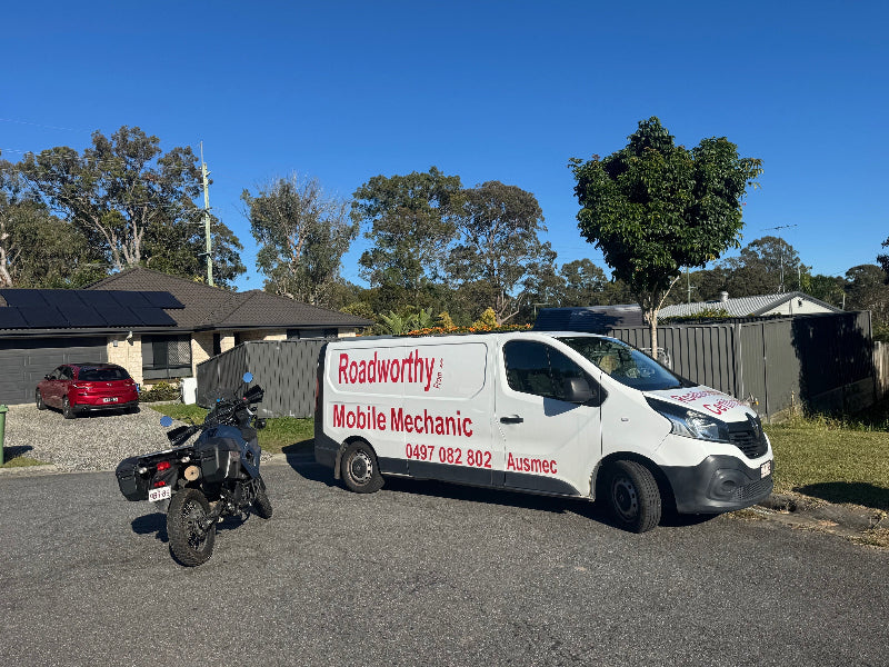 "Motorcycle road test underway as part of a mobile Roadworthy (Safety Certificate) inspection near Alderley." White van with 'Roadworthy Mobile Mechanic' branding parked on a residential street.