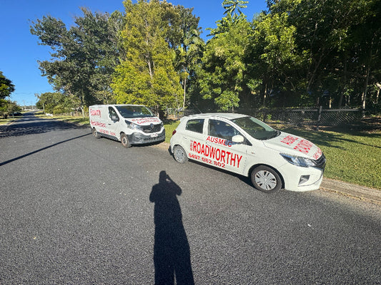 Ausmec vehicles heading to do inspections): Two branded Ausmec Mobile Roadworthy vehicles driving, ready to provide Bridgeman Downs Mobile Roadworthy (Safety Certificate) services directly to customers.
Two vans with branding on a road surrounded by trees