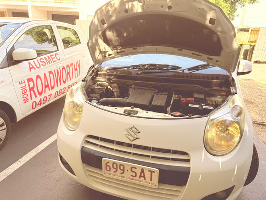 "Our mobile mechanic performing a detailed Caboolture Mobile Roadworthy (Safety Certificate) inspection on a Suzuki Swift." Car with open hood on a road, Ausmec Mobile Roadworthy vehicle in the background.