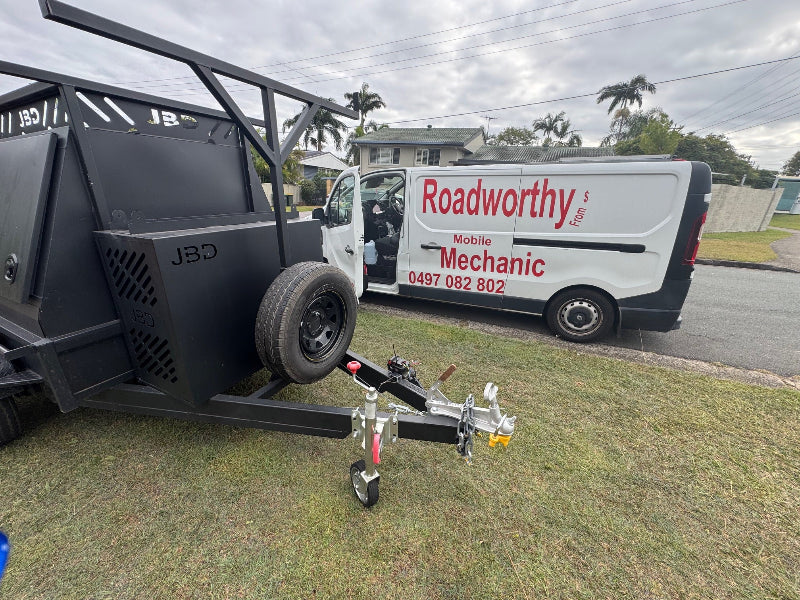 A thorough Cashmere Mobile Roadworthy (Safety Certificate) inspection in progress on a box trailer, conveniently performed on a residential lawn. Trailer attached to a van with 'Roadworthy' branding on a grassy area.