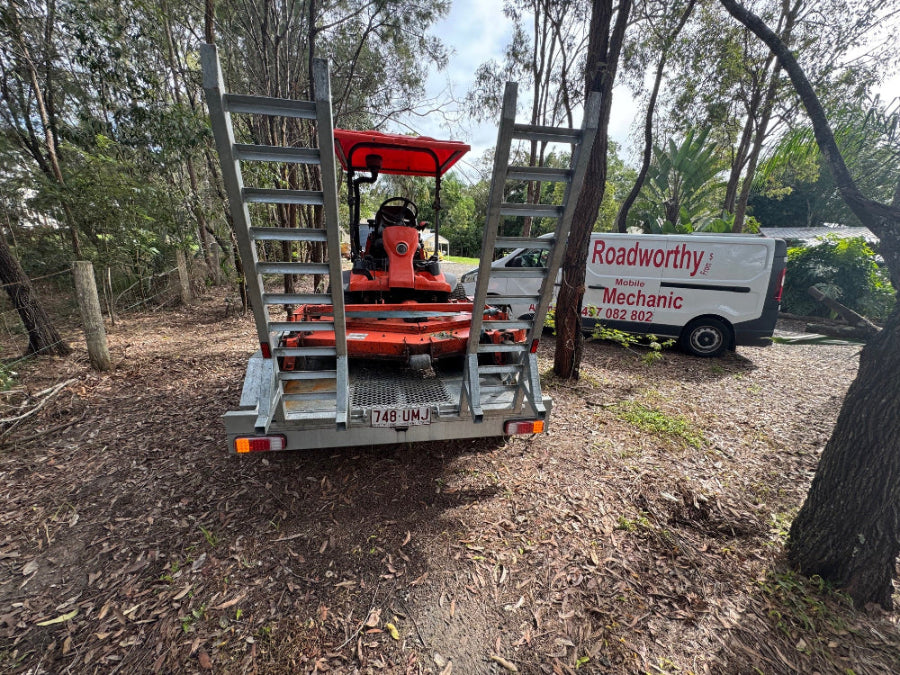 Convenient trailer safety certificate inspection conducted by an Ausmec Mobile Roadworthy inspector at a customer's home in Enoggera. Red lawn mower on a trailer with a 'Roadworthy' van in the background.