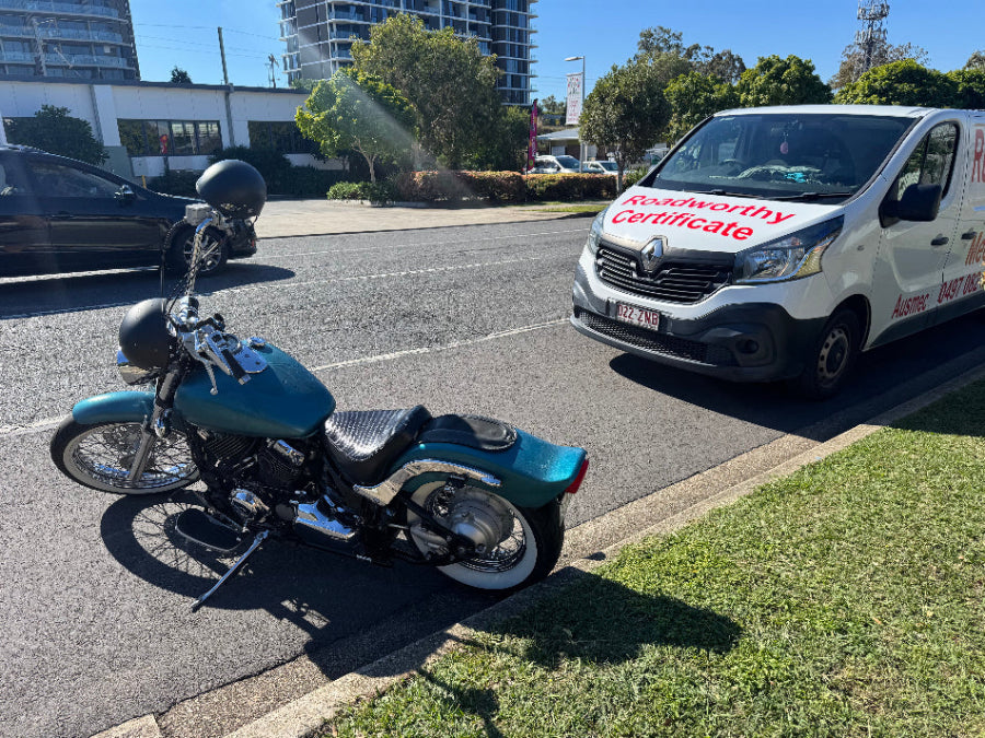 Expert conducting a comprehensive mobile roadworthy inspection on a motorcycle at a customer's location in Everton Hills for their safety certificate. Motorcycle parked on a street with a van in the background