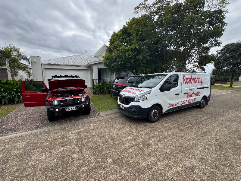 Thorough car inspection in a Ferny Hills customer's driveway for a mobile roadworthy, making your safety certificate process hassle-free. Two vehicles, one with an open hood and the other a white van with branding, parked on a driveway.