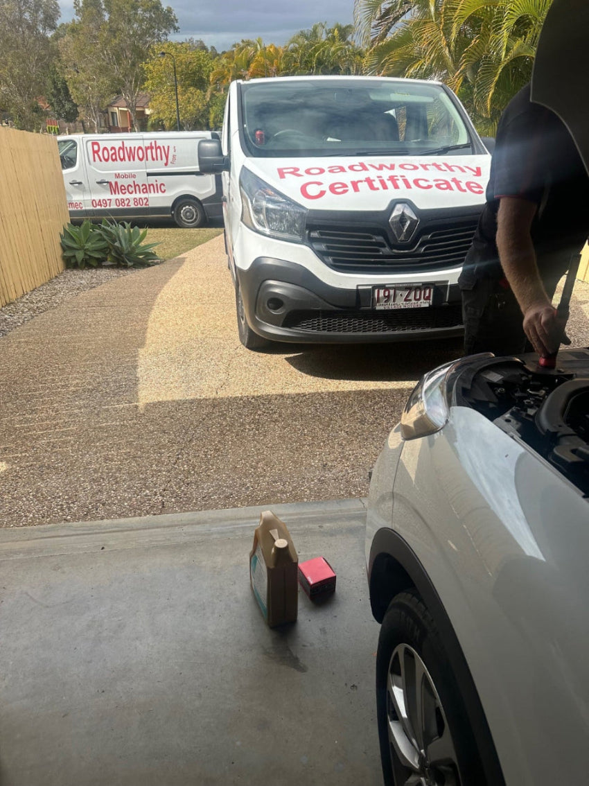 Two Ausmec Mobile Roadworthy vehicles on the way to provide Hamilton Safety Certificate services, offering convenience and expertise. Car with open hood on a driveway, with a van labeled 'Roadworthy Mechanic' in the background.