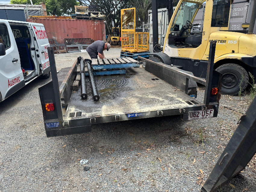 Detailed mobile roadworthy inspection of a trailer being performed at a customer's home in Hendra to get their safety certificate.
Trailer with a flatbed, pipes on a pallet, and a person working in an outdoor setting.