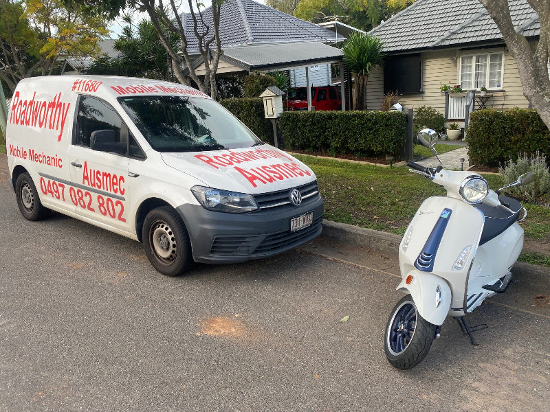 "Licensed mechanic conducting a Kallangur Mobile Roadworthy (Safety Certificate) inspection for a motorcycle or moped to issue an RWC." Van with advertisement text and a scooter on a residential street