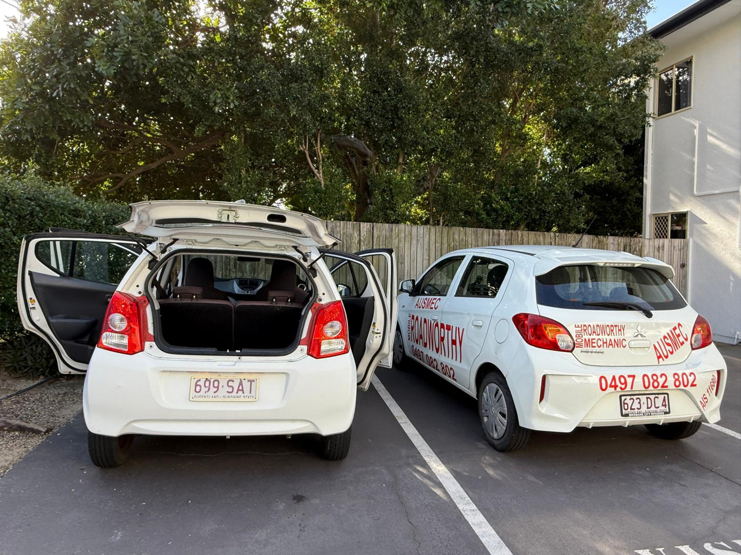 An Ausmec Mobile Roadworthy inspector performs a comprehensive safety certificate inspection on a car in a customer's driveway, highlighting the convenience of our Kippa Ring Mobile Roadworthy (Safety Certificate) service Two white cars with open doors parked on a driveway, one with visible branding.