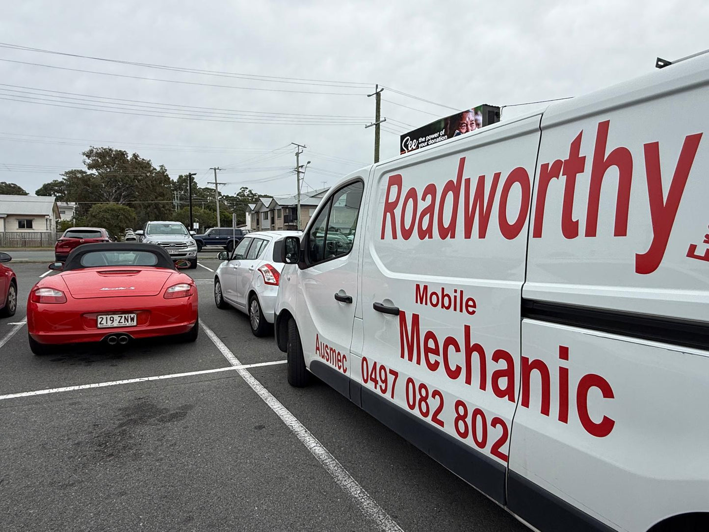 Ausmec Mobile Roadworthy van positioned for a Kurwongbah mobile roadworthy (safety certificate) inspection on a customer's Porsche.
White van with 'Roadworthy' branding on a road with cars in the background