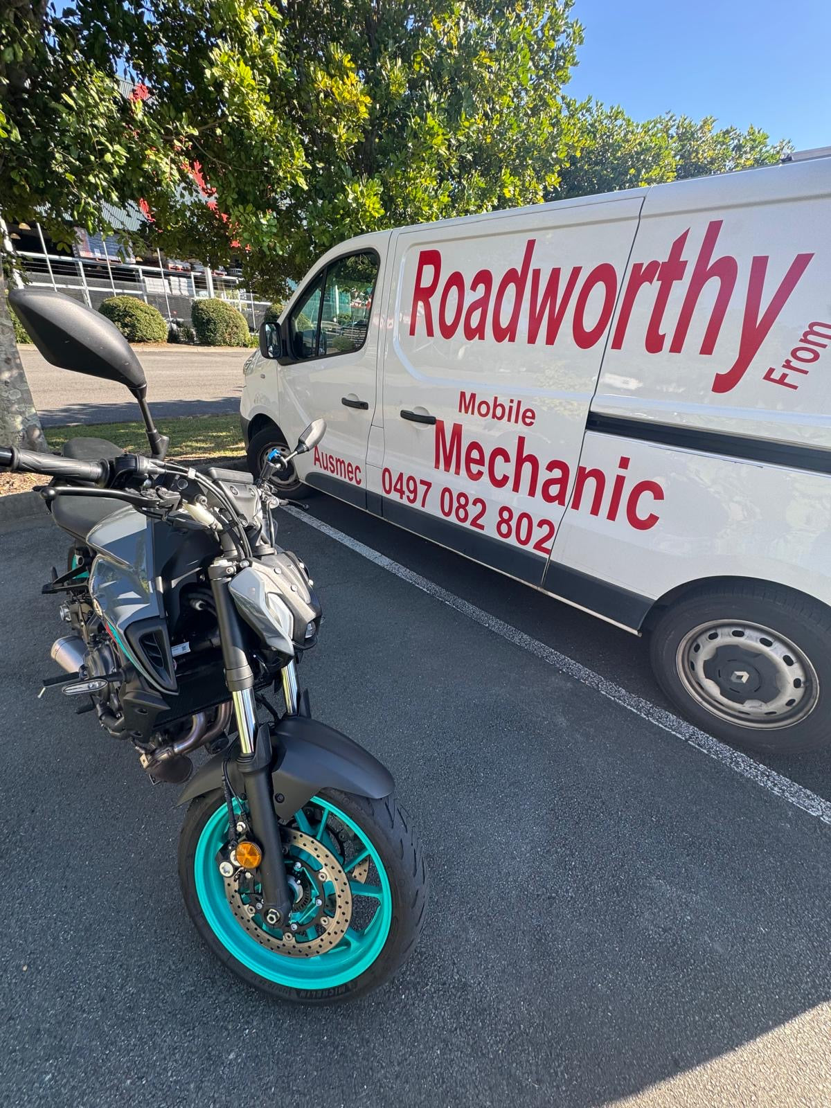 Motorcycle with turquoise wheel parked next to a white van labelled 'Roadworthy Mobile Mechanic' in Sandgate