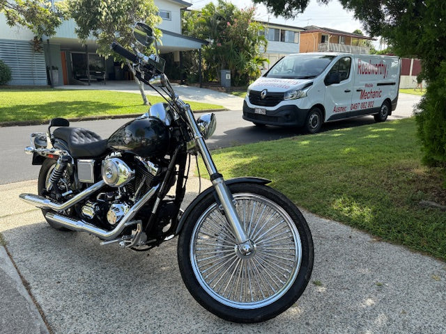 Black motorcycle parked on a driveway with a van in the background in Zillmere