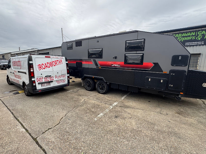 An Ausmec Mobile Roadworthy inspector examining a caravan at a storage unit, demonstrating our versatile mobile roadworthy (safety certificate) service for trailers and caravans in Newport. Van with 'Roadworthy' branding towing a caravan on a concrete surface.