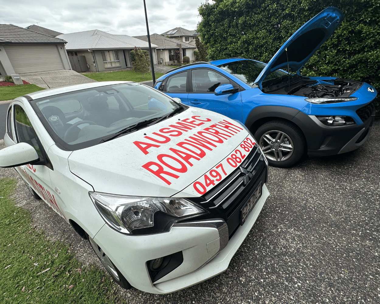 "Blue Hyundai receiving convenient Caboolture South Mobile Roadworthy (Safety certificate) car inspection at customer's home." Two cars, one with 'Ausmee Roadsvc' branding, parked on a residential street.