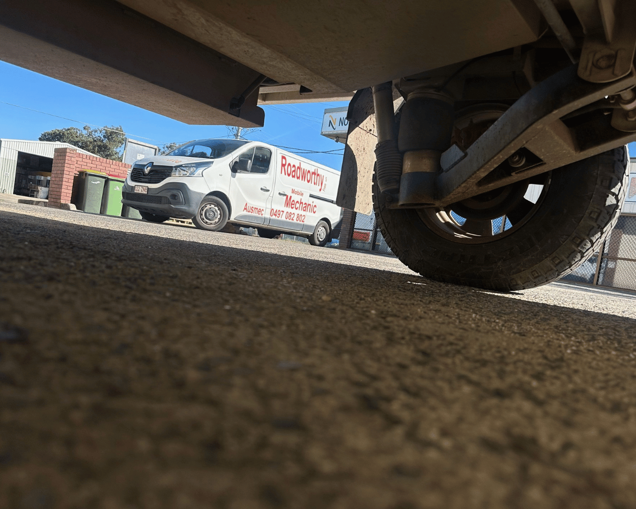 Comprehensive Zillmere Mobile Roadworthy (Safety Certificate) – We provide thorough undercarriage inspections for trailers and caravans, right at your location.Close-up of a vehicle's undercarriage with a van labeled 'Roadworthy Mechanics' in the background.