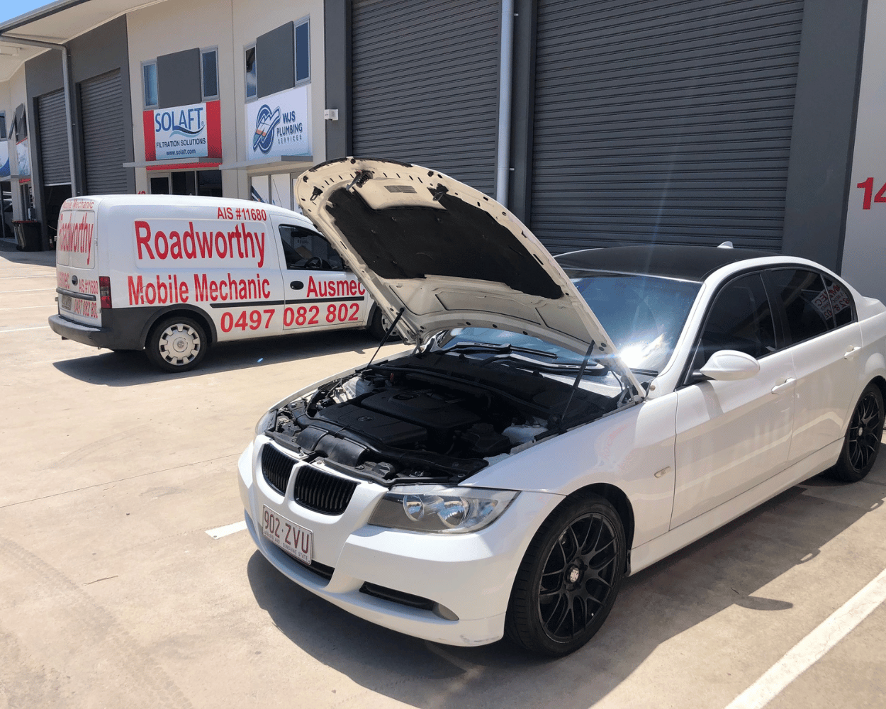 "Ausmec mobile mechanic performing a Narangba Mobile Roadworthy (Safety Certificate) inspection on a BMW car in a customer's car park." White car with open hood in front of a van labeled 'Roadworthy Mobile Mechanic'