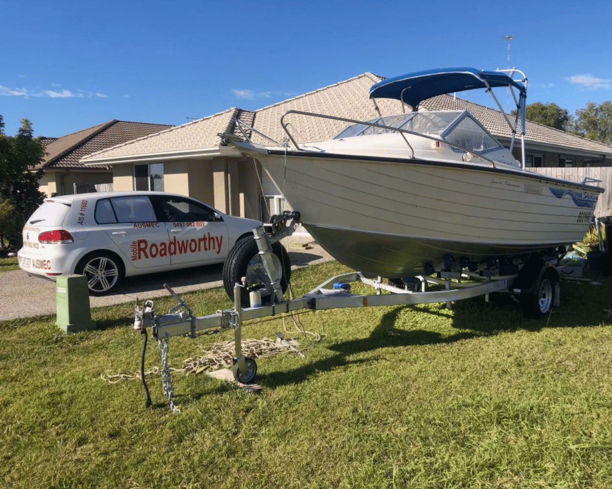 "Boat trailer undergoing a Scarborough Mobile Roadworthy (Safety Certificate) inspection at a customer's home, with a VW Golf Alltrack nearby." Boat on a trailer in front of a house with a 'Roadworthy' vehicle in the background.