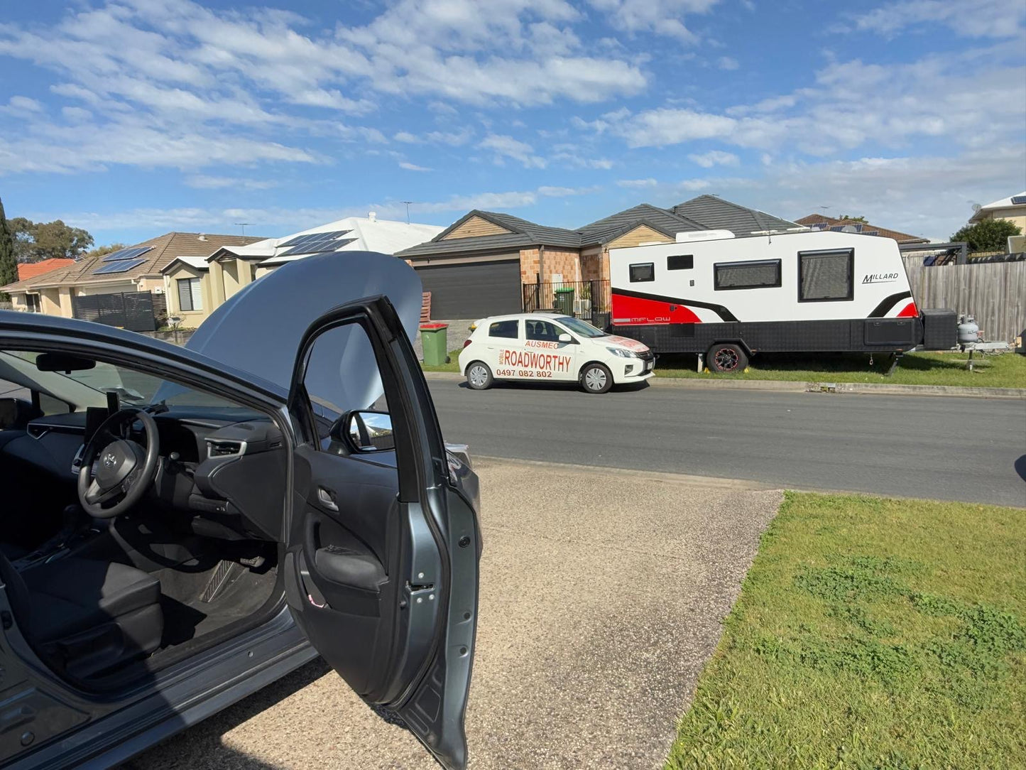 Detailed pre-purchase car inspection near Brisbane with the bonnet and doors open for a comprehensive check of all vehicle components. Car with open door on a driveway, caravan in the background