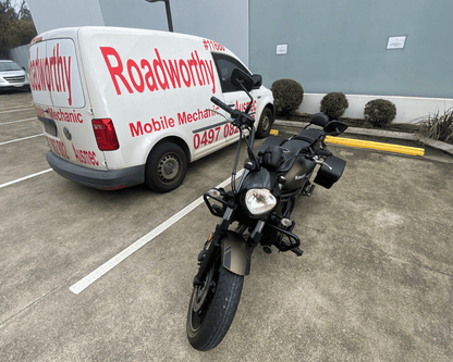 "Ausmec mobile inspection van on-site, with a motorcycle receiving its Bellmere Mobile Roadworthy (Safety Certificate) inspection." White van with 'Roadworthy' branding and a motorcycle in a parking lot.