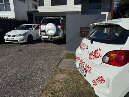 "Two cars in Bellmere undergoing Bellmere Mobile Roadworthy (Safety Certificate) inspections in a customer's driveway for interstate registration transfer." Two cars parked in a driveway with a close-up of a white car's rear end showing 'AUSMEC' branding.