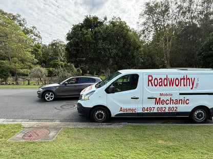 An Ausmec Mobile Roadworthy inspector conducting a thorough test drive of a car as part of an Ascot Mobile Roadworthy (Safety Certificate) inspection. White van with 'Roadworthy Mobile Mechanic' branding parked on a road with trees in the background.