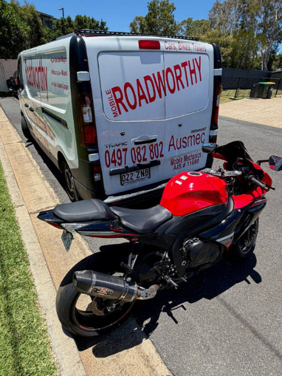 Van with 'Roadworthy' branding next to a red motorcycle on a residential street in Enoggera.