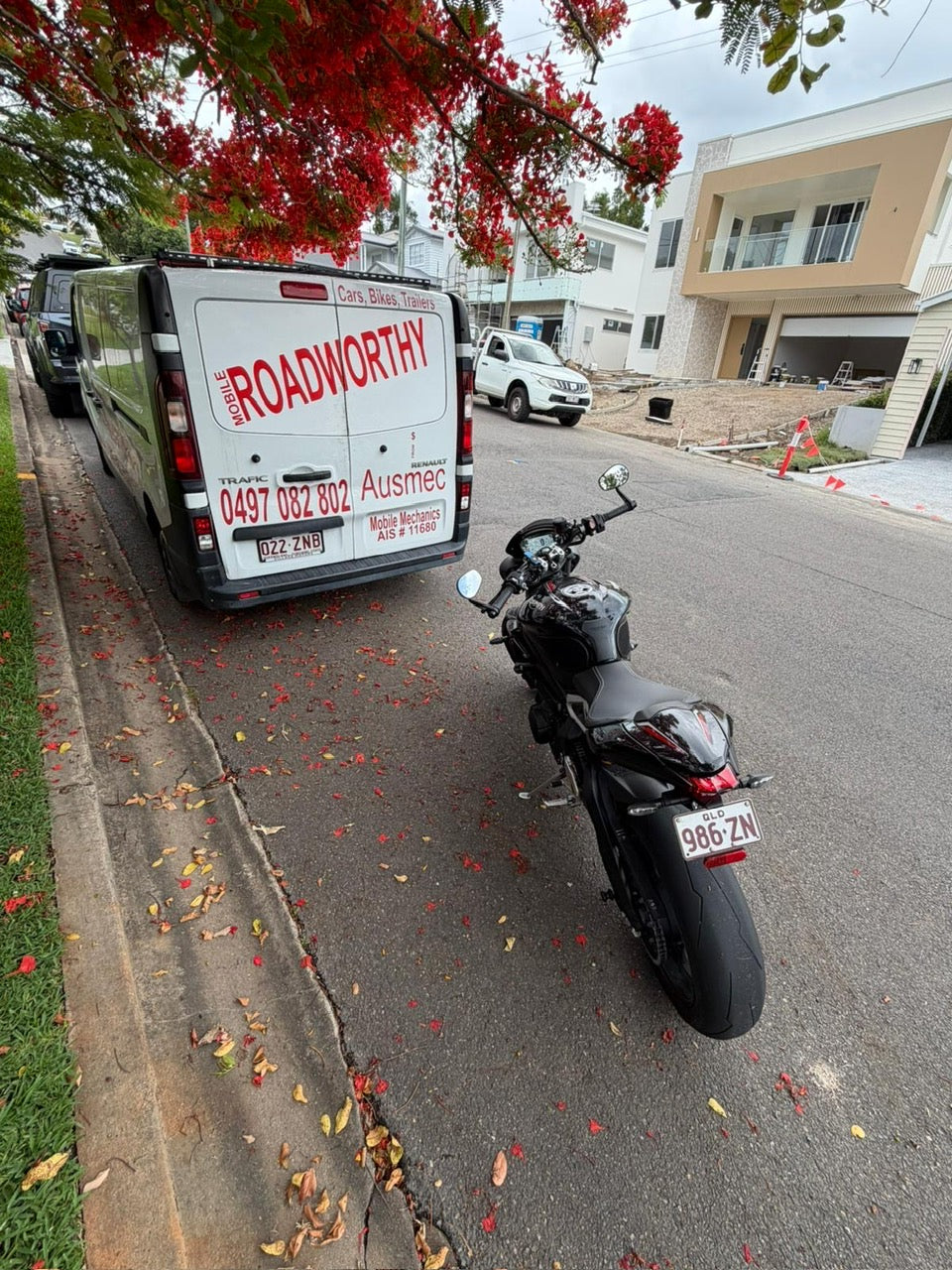 Motorcycle parked on a residential street next to a van with 'Roadworthy' branding in Enoggera.
