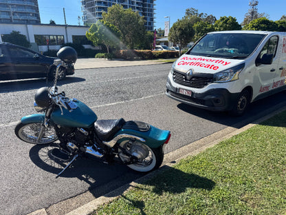 Expert conducting a comprehensive mobile roadworthy inspection on a motorcycle at a customer's location in Everton Hills for their safety certificate. Motorcycle parked on a street with a van in the background