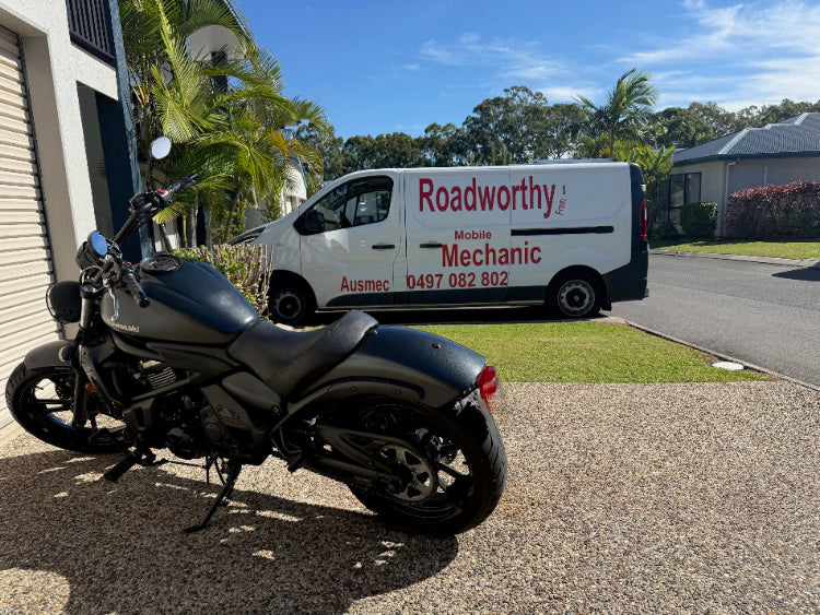 Black motorcycle parked on a driveway with a van labeled 'Roadworthy' in the background in Everton Hills