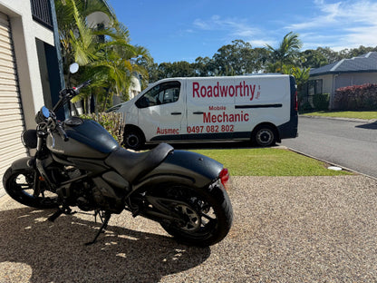 Black motorcycle parked on a driveway with a van labeled 'Roadworthy' in the background in Everton Hills