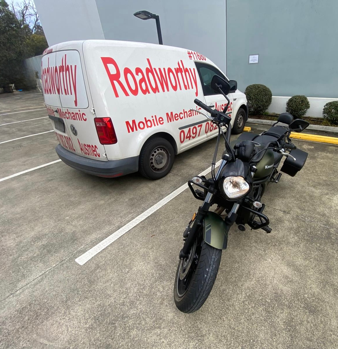 White Roadworthy Inspection Van with red branding parked next to a motorcycle in a parking lot in Grange.