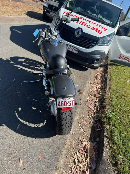 Motorcycle parked on the side of a road with a white van in the background displaying a 'Roadworthy Certificate' in Hendra