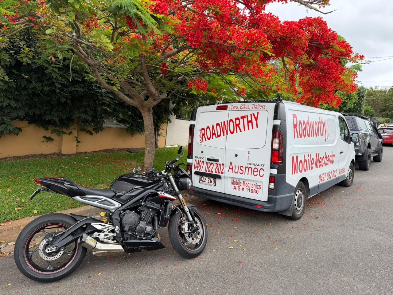 Roadworthy mobile mechanic van parked next to a motorcycle on a street with trees in the background in Kedron.