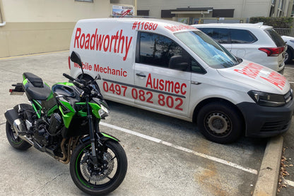 "Motorcycle undergoing a thorough Burpengary Mobile Roadworthy (Safety Certificate) inspection in a parking bay." White van with red text and a motorcycle on a concrete surface