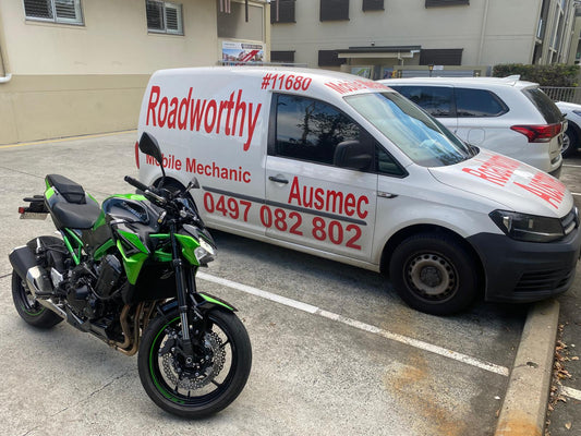 White Mobile Roadworthy Van with red text and a green motorcycle in front of a building in Alderley