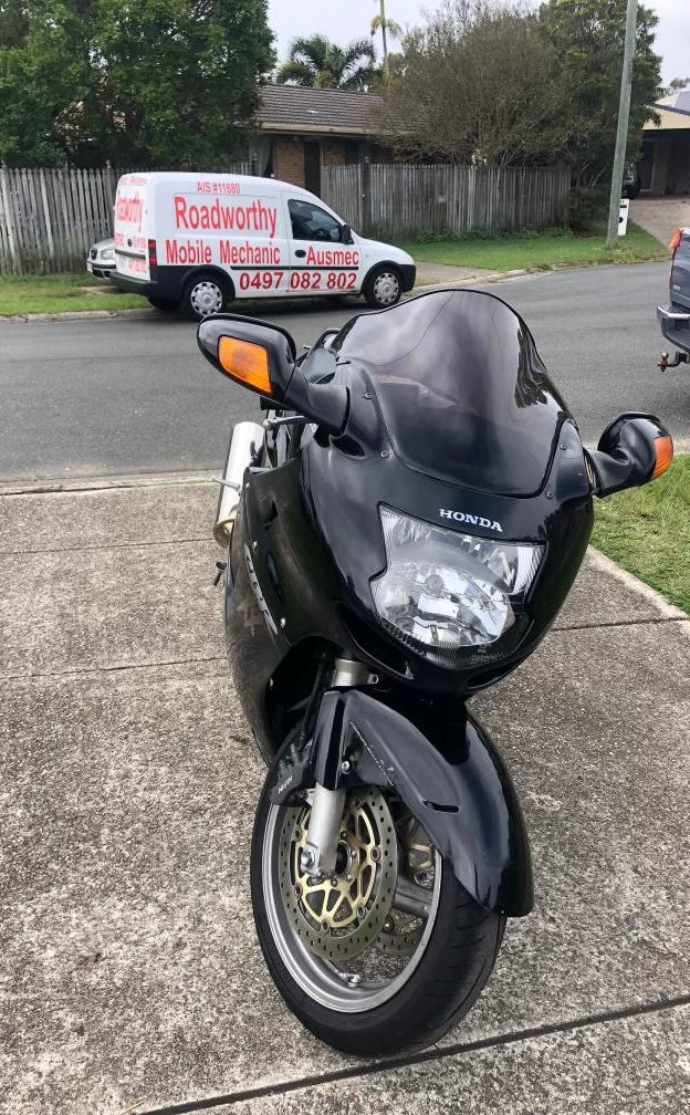 Black Honda motorcycle parked on a driveway with a Roadworthy Van in the background on a street in Geebung.