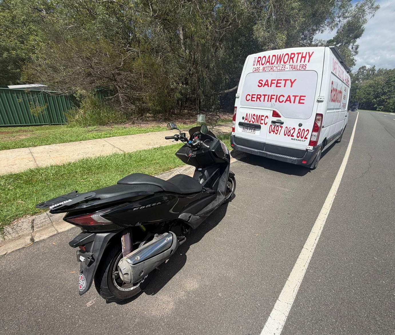 Black scooter parked on a road next to a white van with safety certificate branding in Taigum.