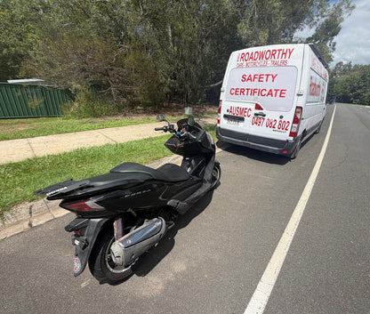 Black scooter parked on a road next to a white van with safety certificate branding in Taigum.