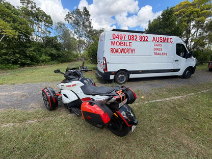White van with red text 'Mobile Roadworthy' parked on grass next to a three-wheeled motorcycle in Mitchelton