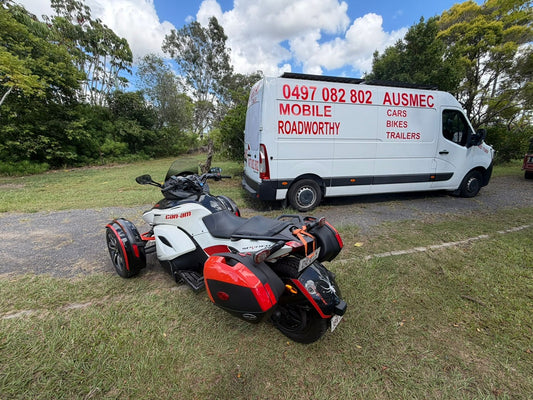 White van with red text 'Mobile Roadworthy' parked on grass next to a three-wheeled motorcycle in Mitchelton
