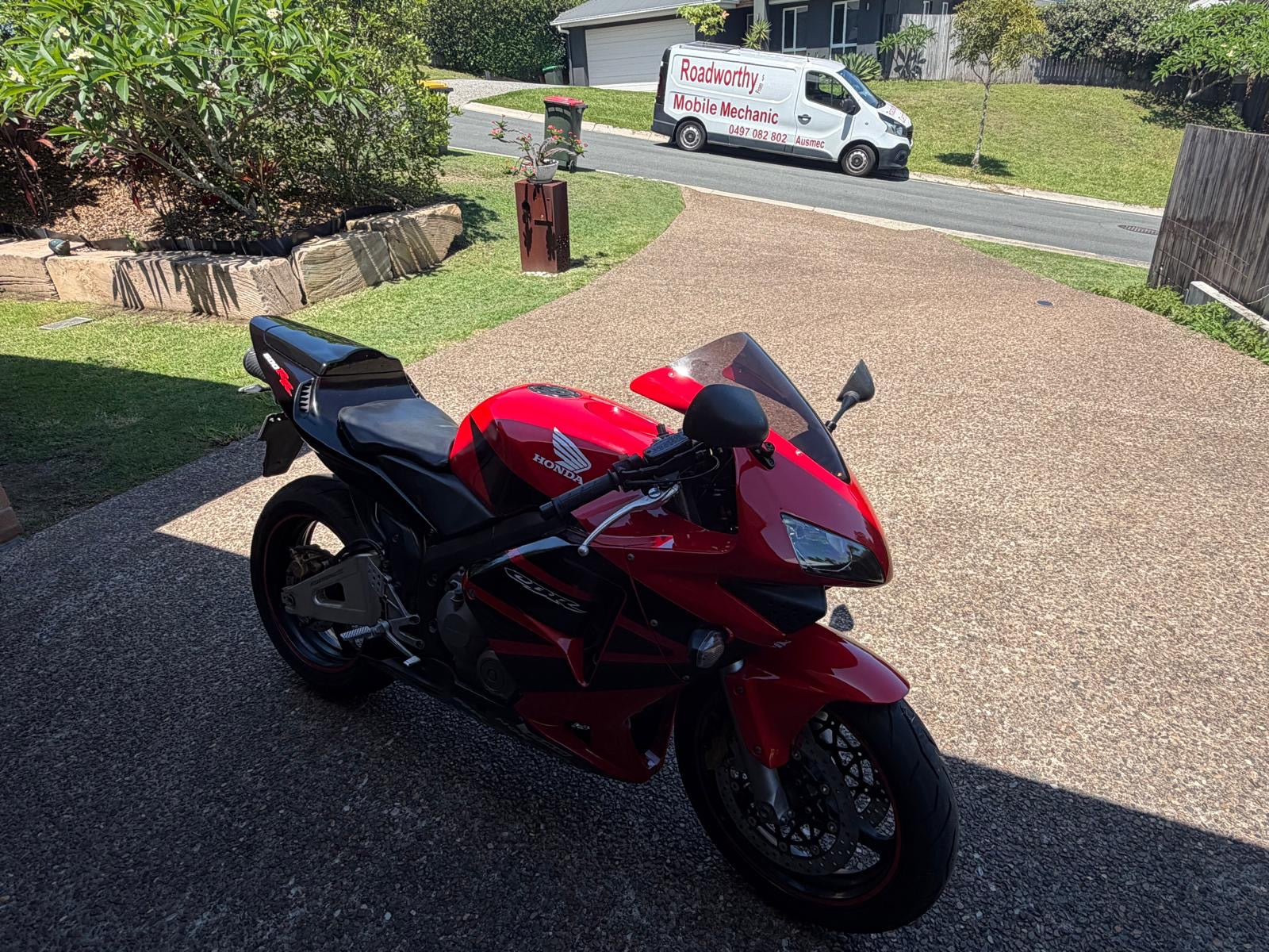 Red motorcycle with a Roadworthy Inspection Van in the background in a residential area in Pinkenbah