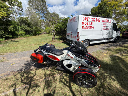 White and red three-wheeled vehicle parked next to a white van with text on the side 'Mobile Roadworthy' in Redcliffe