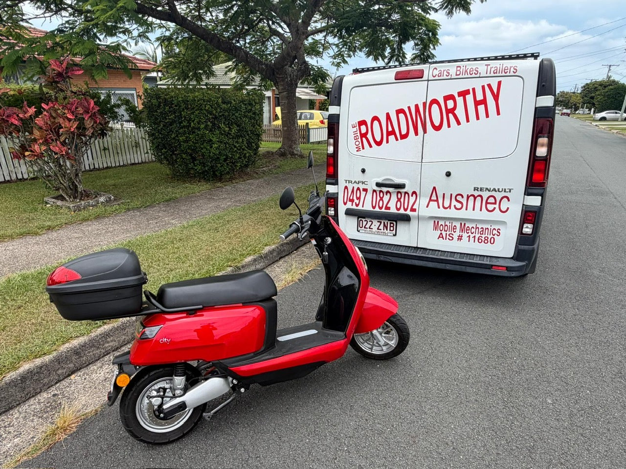 Red scooter parked on a street with a van labeled 'Roadworthy Ausmec' in the background in Lawnton