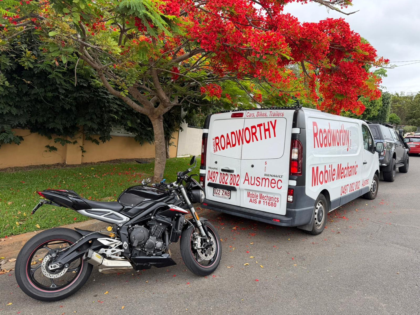 Roadworthy mobile mechanic van parked next to a motorcycle on a street with trees in the background in Nundah.