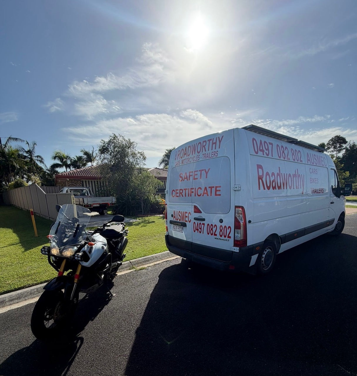White van with 'Roadworthy' branding parked on a residential street with a motorcycle nearby in Nudgee