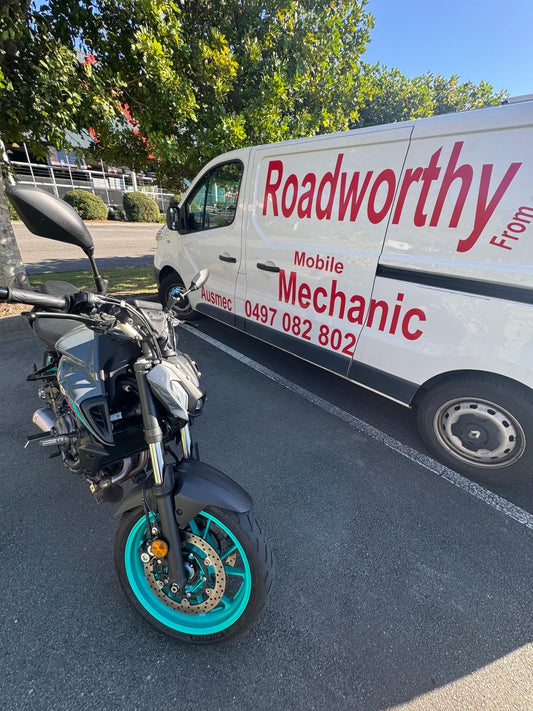 Motorcycle with turquoise wheel parked next to a white van labelled 'Roadworthy Mobile Mechanic' in Nudgee