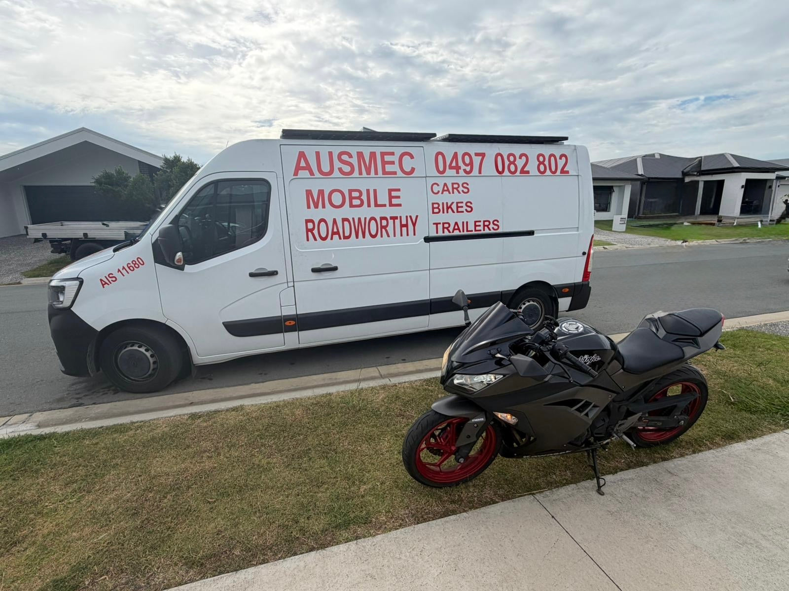 White van with red text parked on a residential street next to a motorcycle in Petrie
