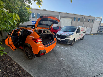 Orange SUV with open trunk in a parking lot with a white van in the background. An expert mobile mechanic from Ausmec meticulously checks a car with the bonnet and doors open for a pre-purchase car inspection near Deagon.