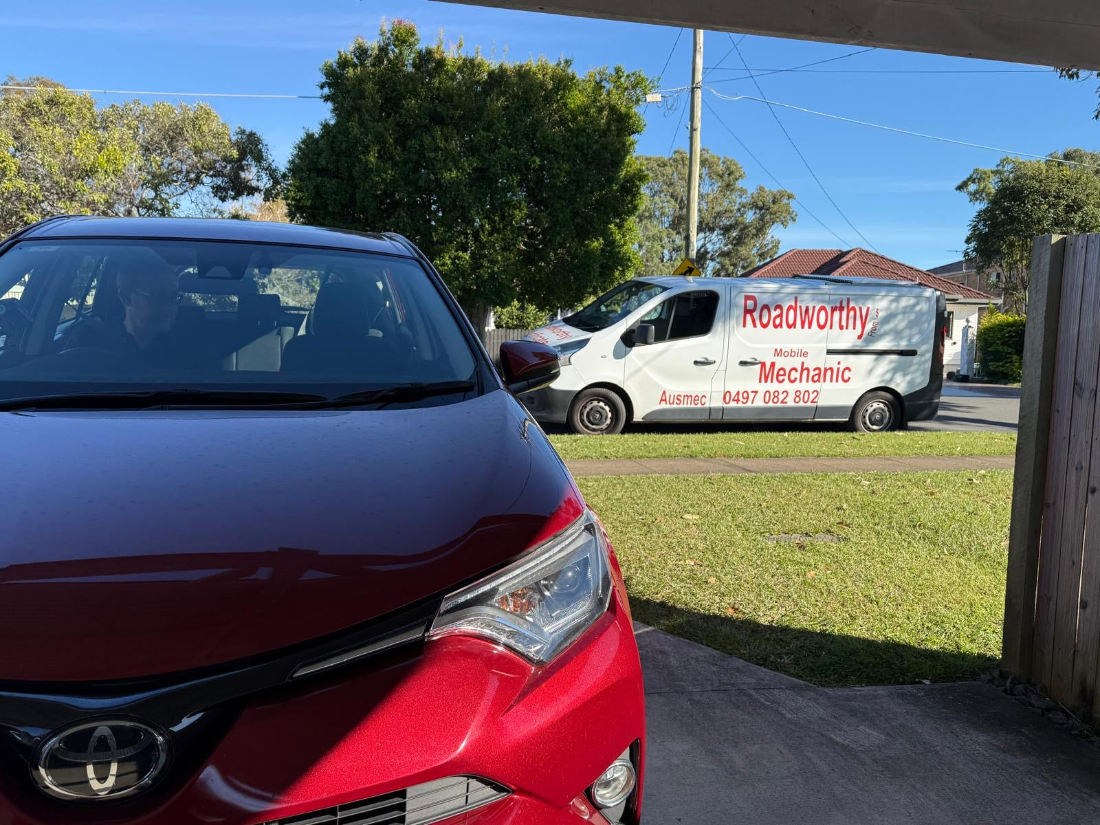 An Ausmec mechanic conducting a pre-purchase car inspection on a used car situated on the grass at a private seller's residence in Narangba.
Red car parked on a driveway with a Roadworthy van in the background.