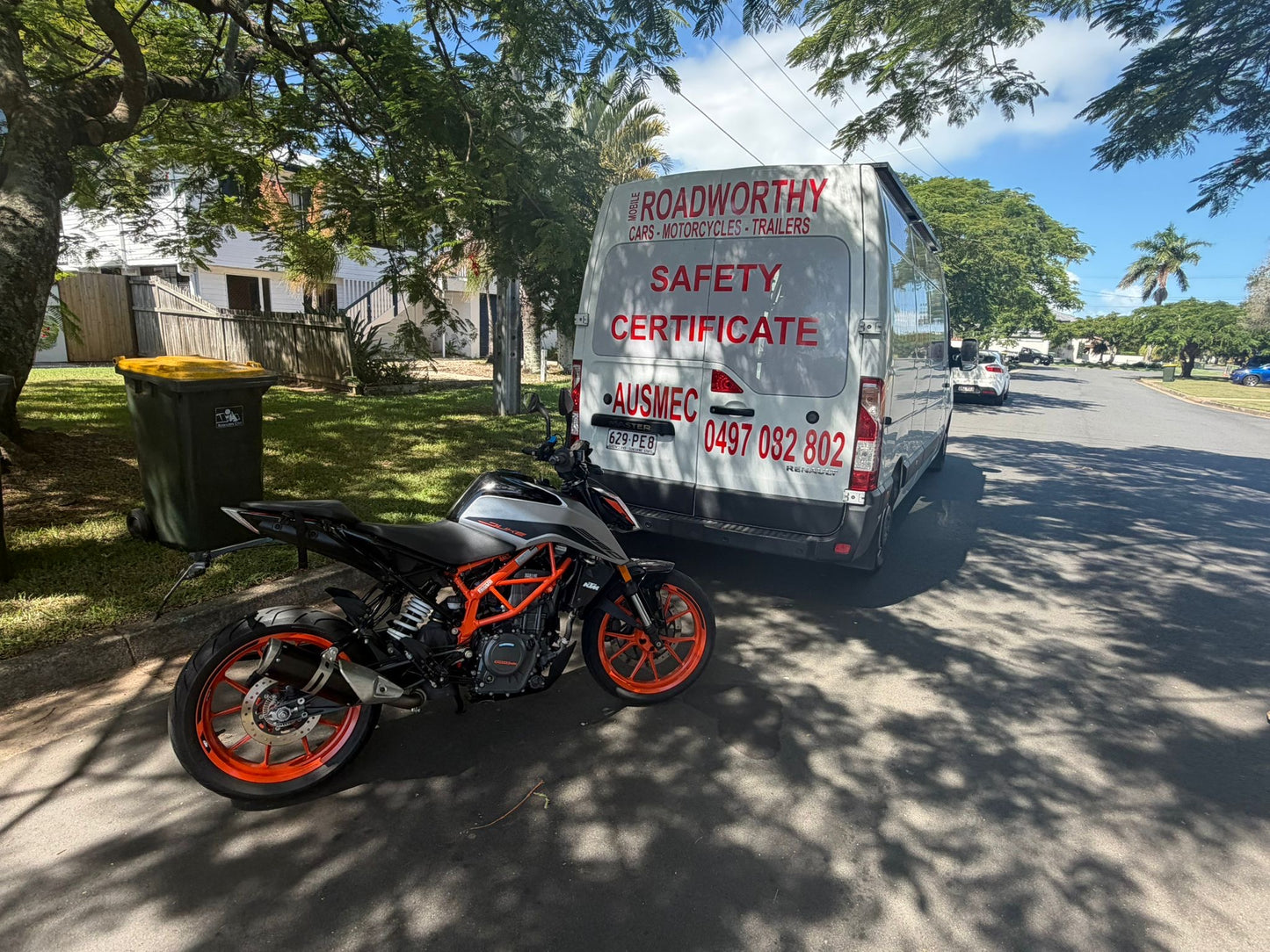 Motorcycle parked on a street next to a van with 'Roadworthy Safety Certificate' branding in Redcliffe.