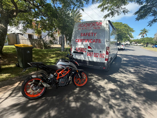 Motorcycle parked on a street next to a van with 'Roadworthy Safety Certificate' branding in Redcliffe.