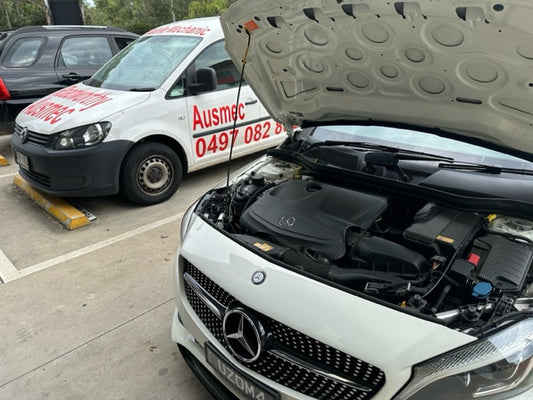 A white Mercedes-Benz with its bonnet open is being inspected by a North Lakes Mobile Roadworthy (Safety Certificate) mechanic. Our mobile inspection van is visible in the background, ready to provide convenient service.